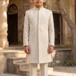 Young boy wearing an off-white plain silk sherwani with elegant digital thread embroidery and matching trousers.